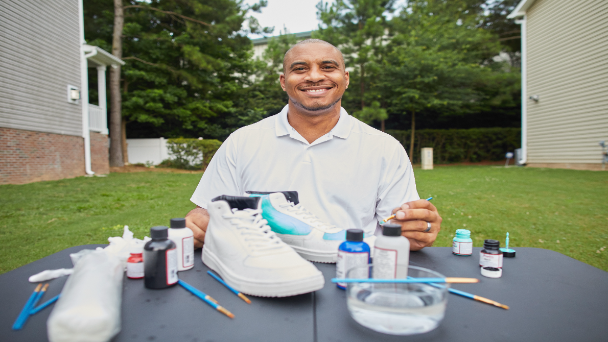 a smiling man standing in front of a table with materials for craft making